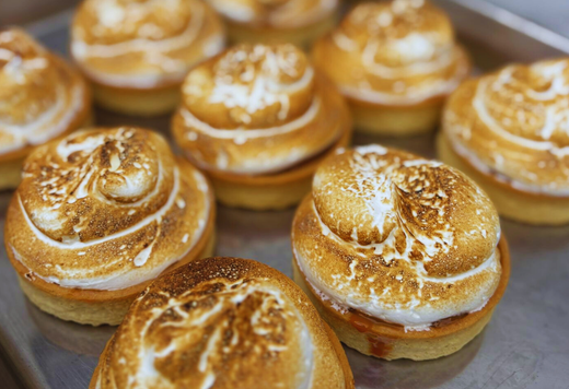 a close up of a tray of cakes with meringue in tart cases on a silver tray