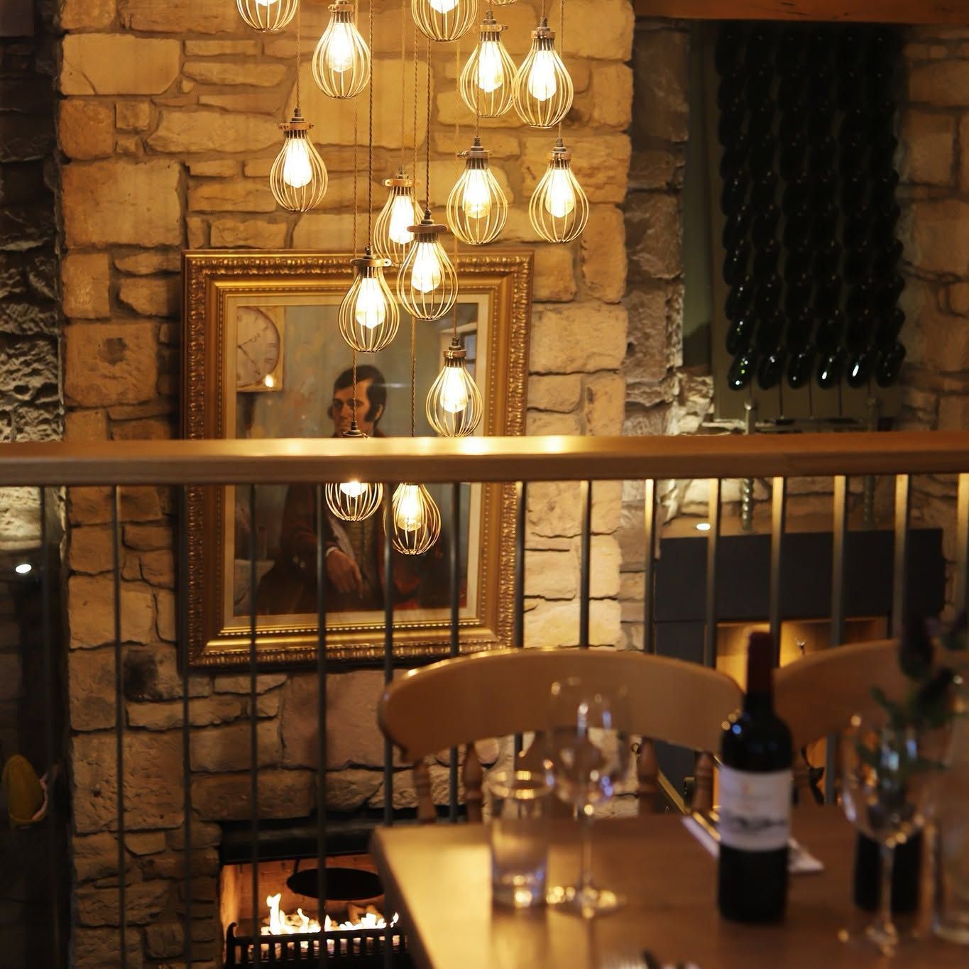 Cozy stone-walled café with hanging lights, a mirror, and a table with wine and glasses