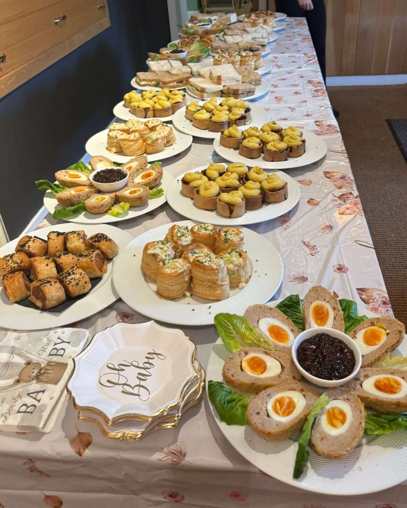 Buffet table with assorted pastries, cookies, and decorated desserts on white platters and a floral tablecloth