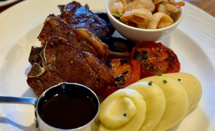 Plated grilled meat with sauce, sliced potatoes, and a side bowl of prawns