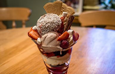 Strawberry and vanilla ice cream sundae in a glass, topped with wafers and chocolate, on a wooden table.