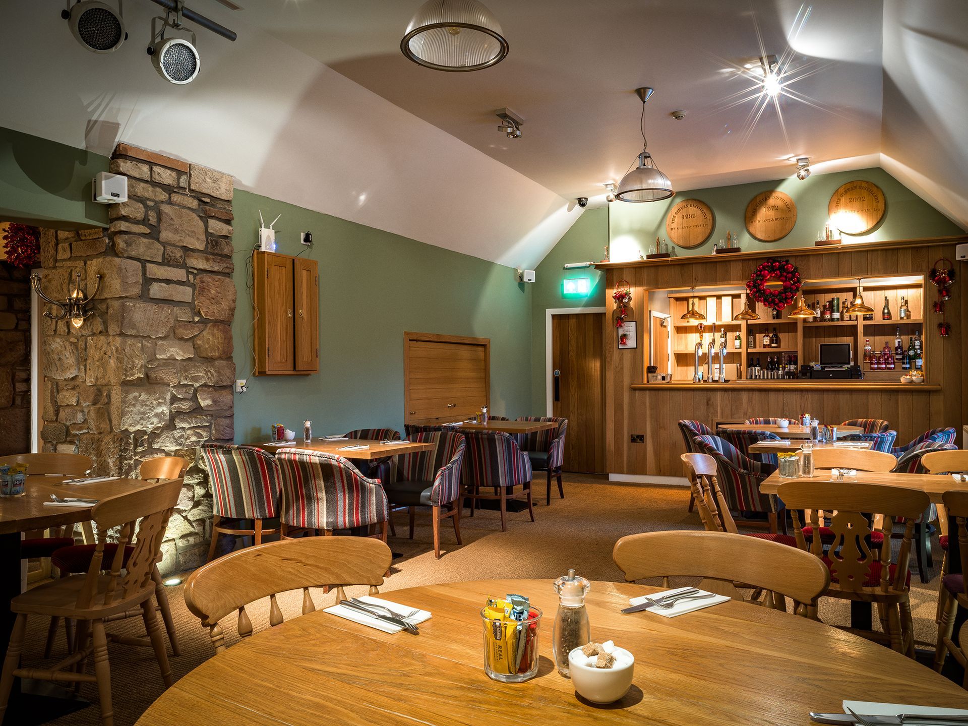 an image showing a cozy rustic restaurant interior with wooden tables, stone wall, arched ceiling, and warm hanging lights