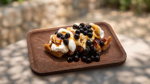 Dessert topped with whipped cream and blueberry sauce on a wooden tray outdoors