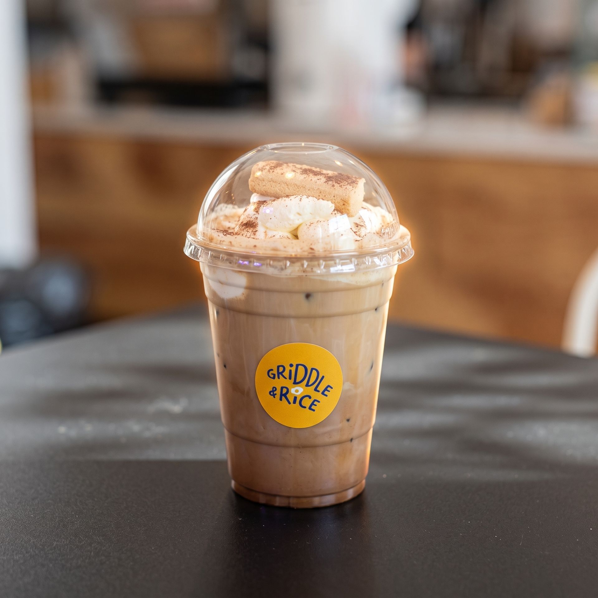 Iced coffee in a clear plastic cup with a domed lid and yellow logo on a table