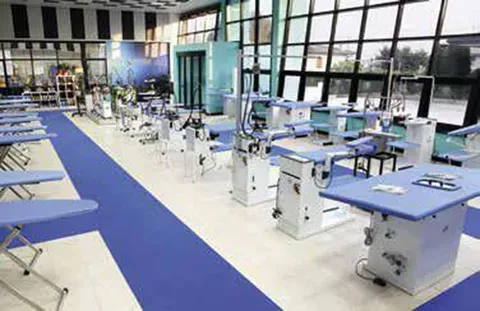 Aula moderna con banchi blu, pavimenti bianchi e grandi finestre in un luminoso laboratorio tecnologico.