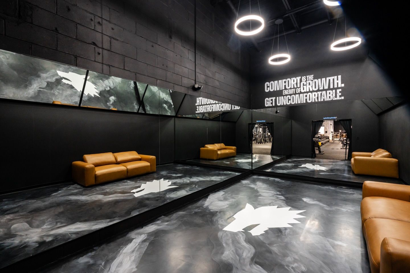 Modern black lounge with tan sofas, concrete floor, and neon ring lights on the ceiling