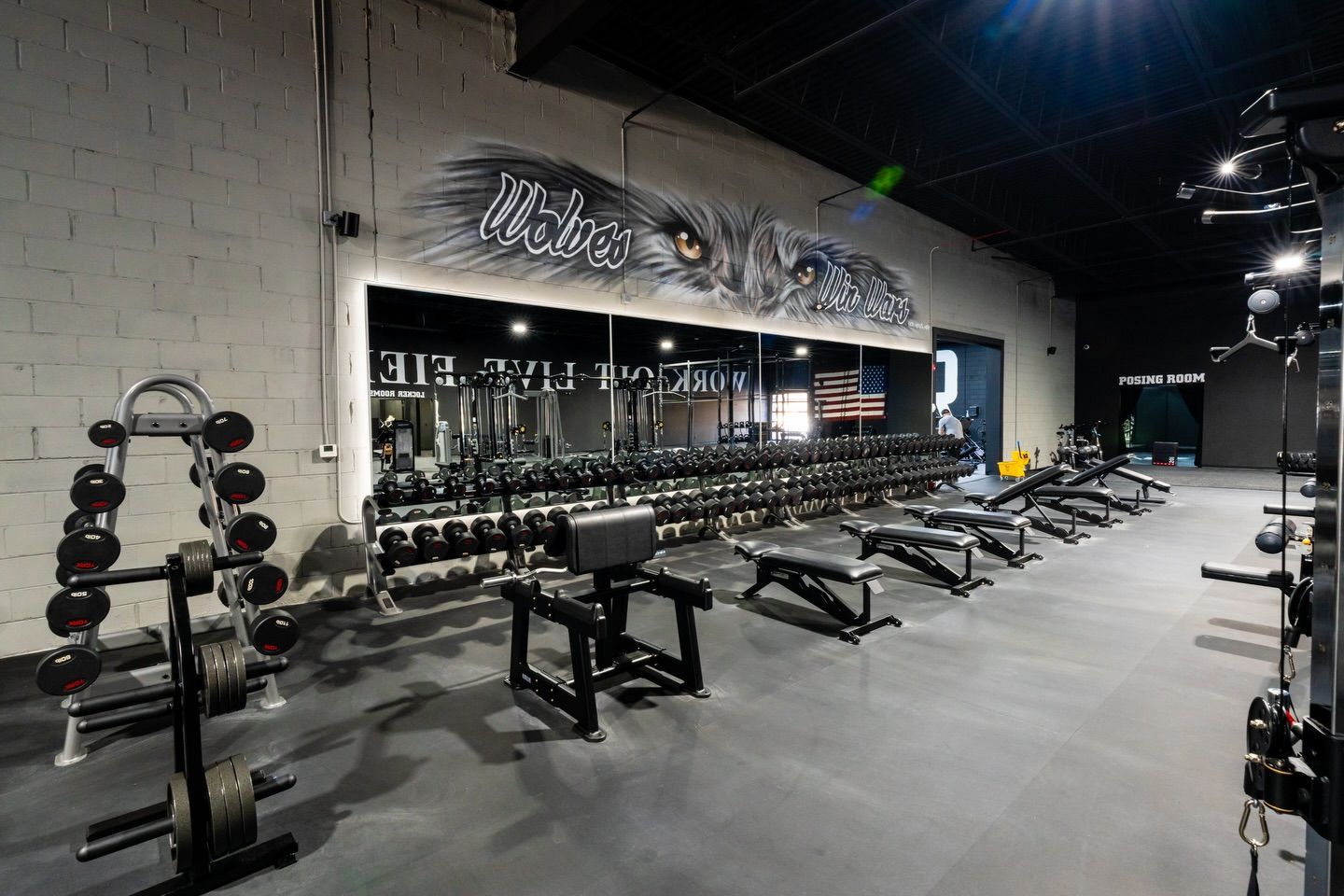 Modern gym interior with dumbbells, weight benches, and mirrors along a concrete wall