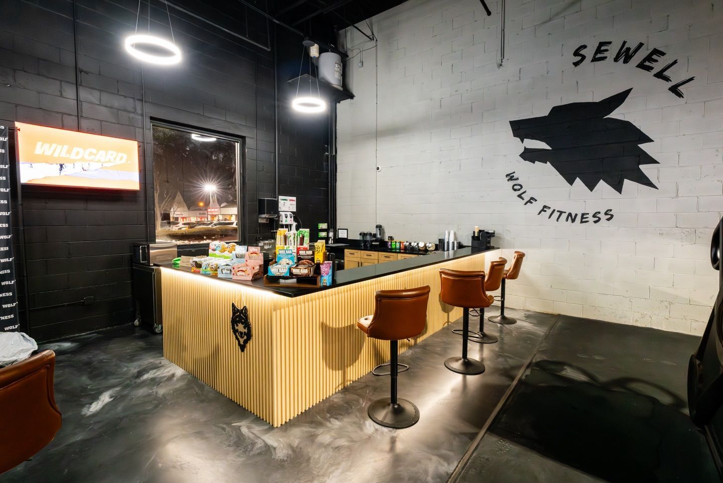 Modern bar counter with stools in a gym-themed interior featuring the Sewell logo on the wall