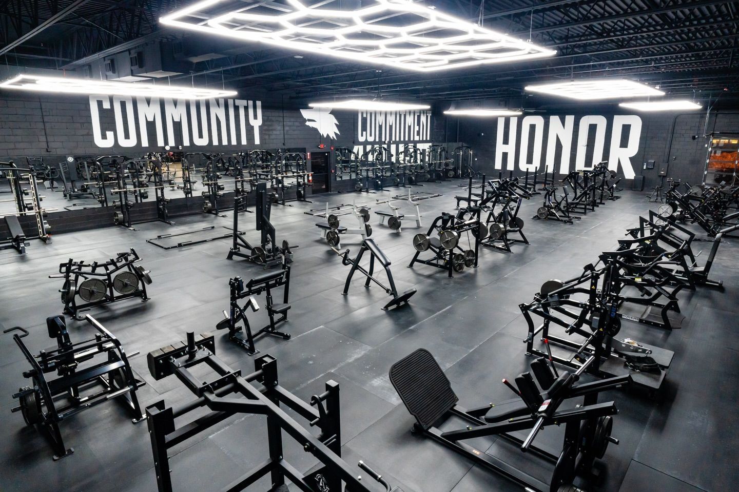 Modern gym with weight machines, neon ceiling lights, and wall words “COMMUNITY,” “UNITY,” and “HONOR.”