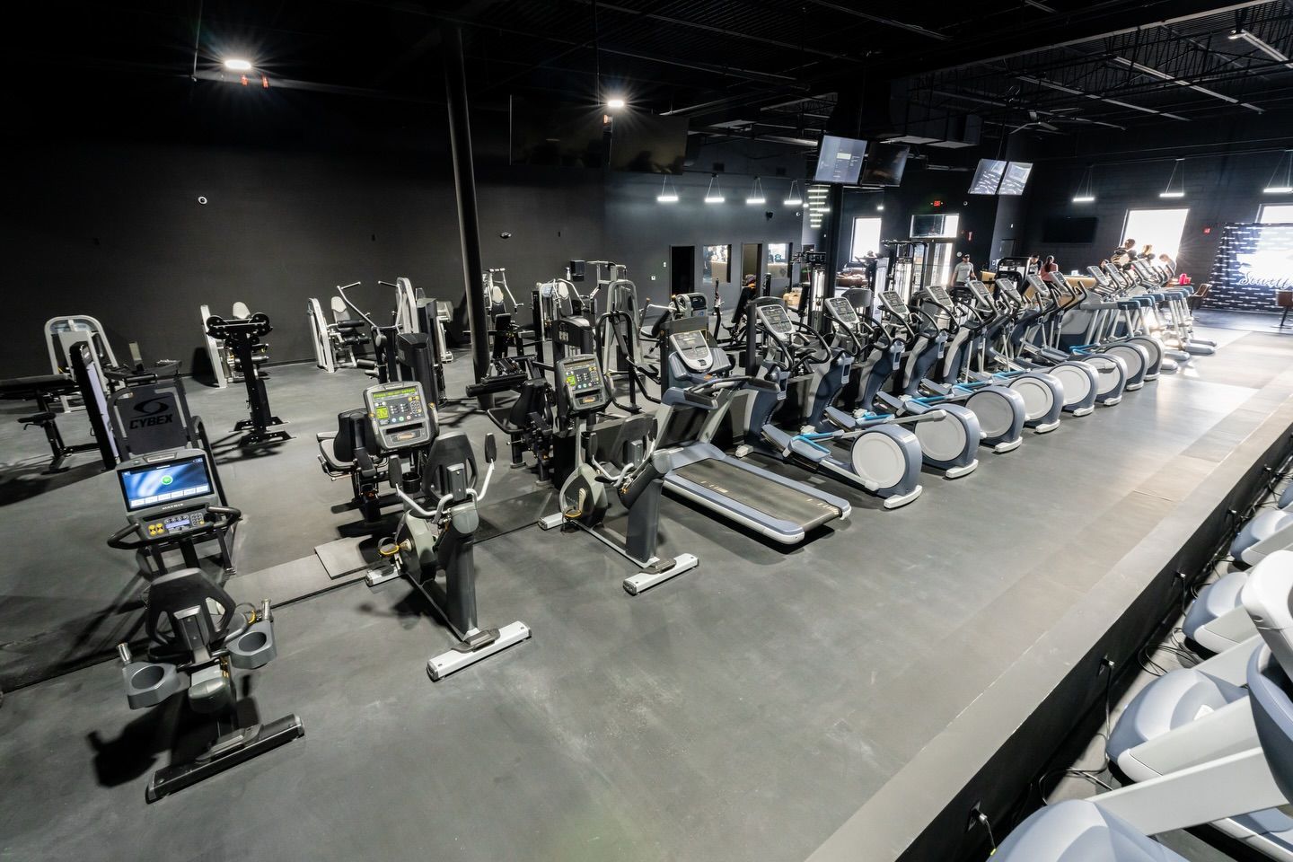Rows of exercise bikes and gym machines in a spacious, dimly lit fitness center