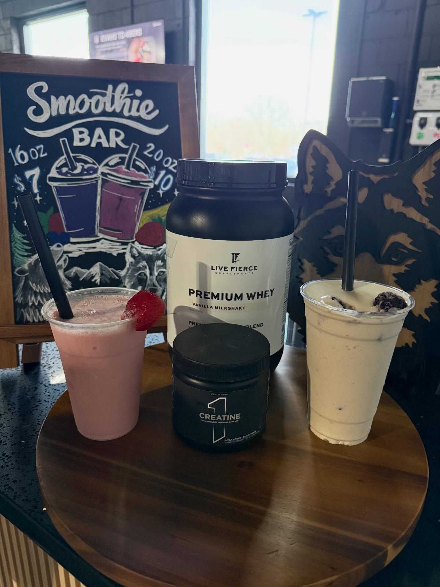 Smoothie bar display with two colorful drinks and a white protein whey container on a table