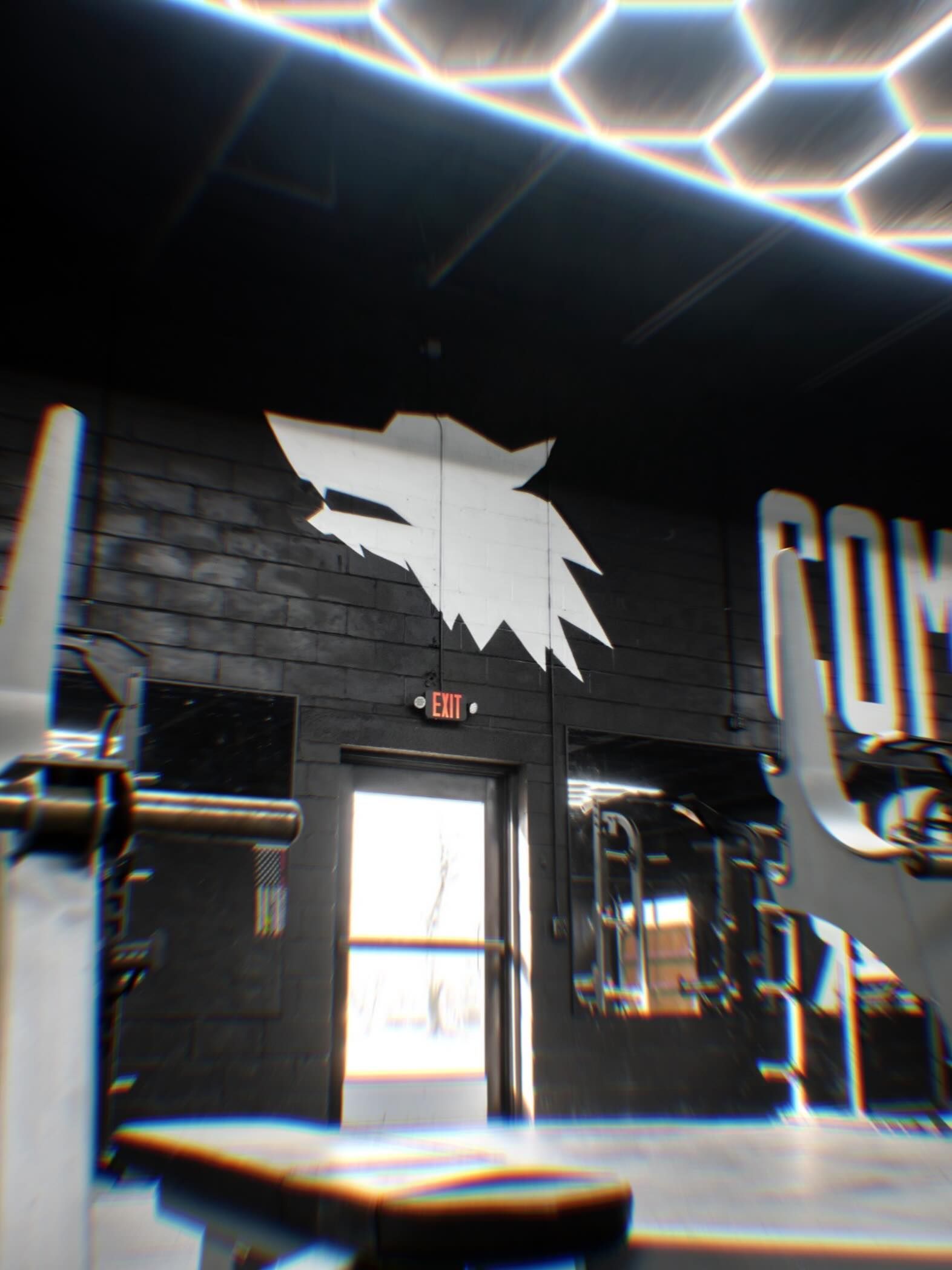 Dim gym interior with black brick walls, weight bench, and barbells under bright overhead lights.