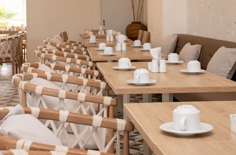 Una fila de mesas y sillas en un restaurante con tazas y platillos sobre ellas en Ciela Hotel