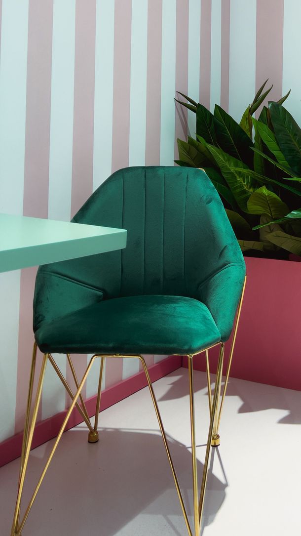 Teal upholstered chair with gold legs beside a mint table and potted plant in a pastel room