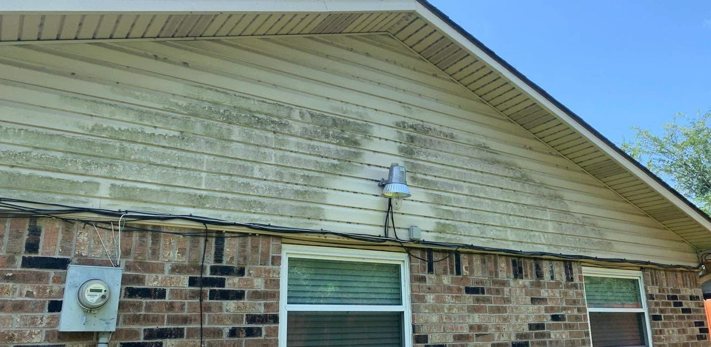 Brick house exterior with white siding, roof overhang, utility meter, and window.