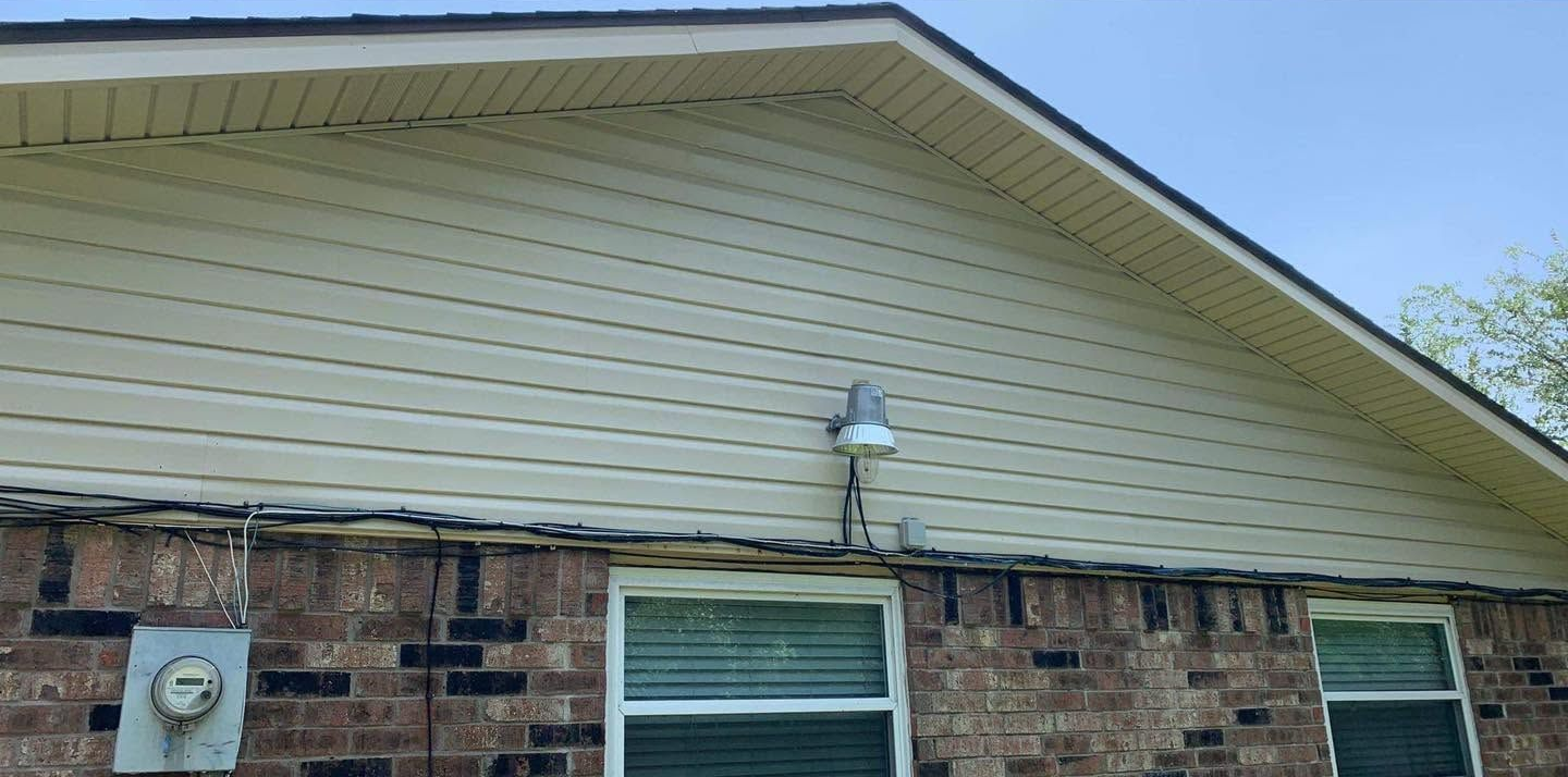 Brick house exterior with beige siding, a window, and a wall-mounted light under the roofline