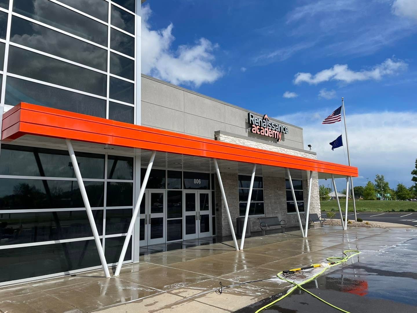 Storefront entrance with orange awning, wet sidewalk, and flags outside under a blue sky