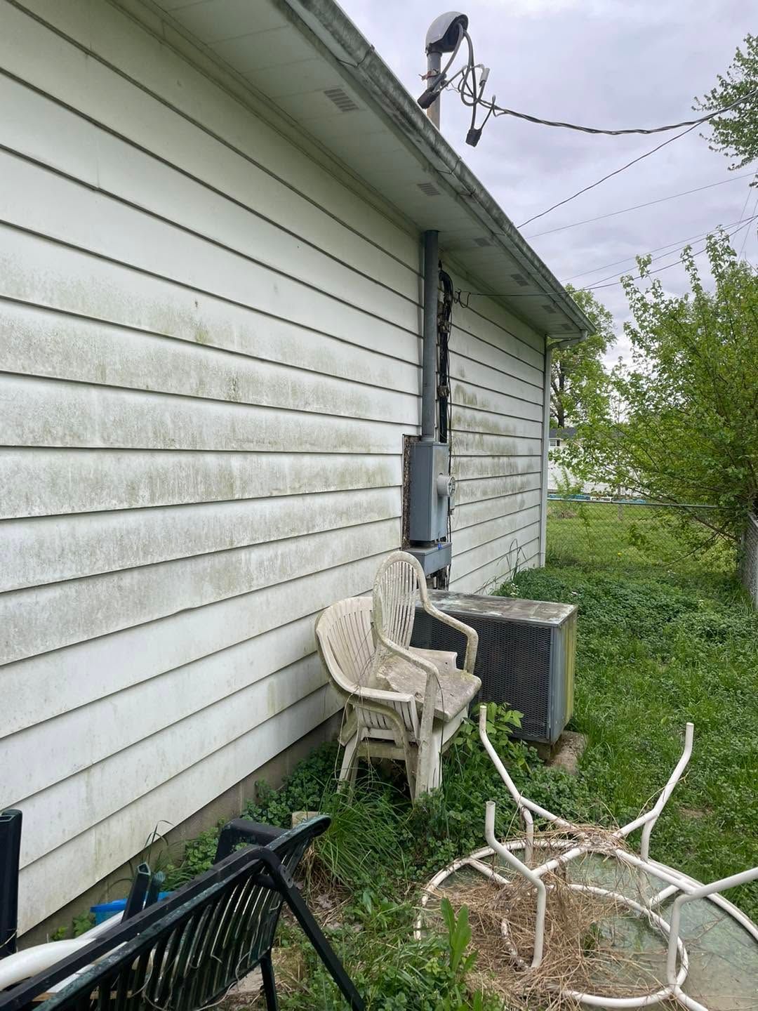 Side of a white house with two chairs, an AC unit, and fallen branches in a yard.
