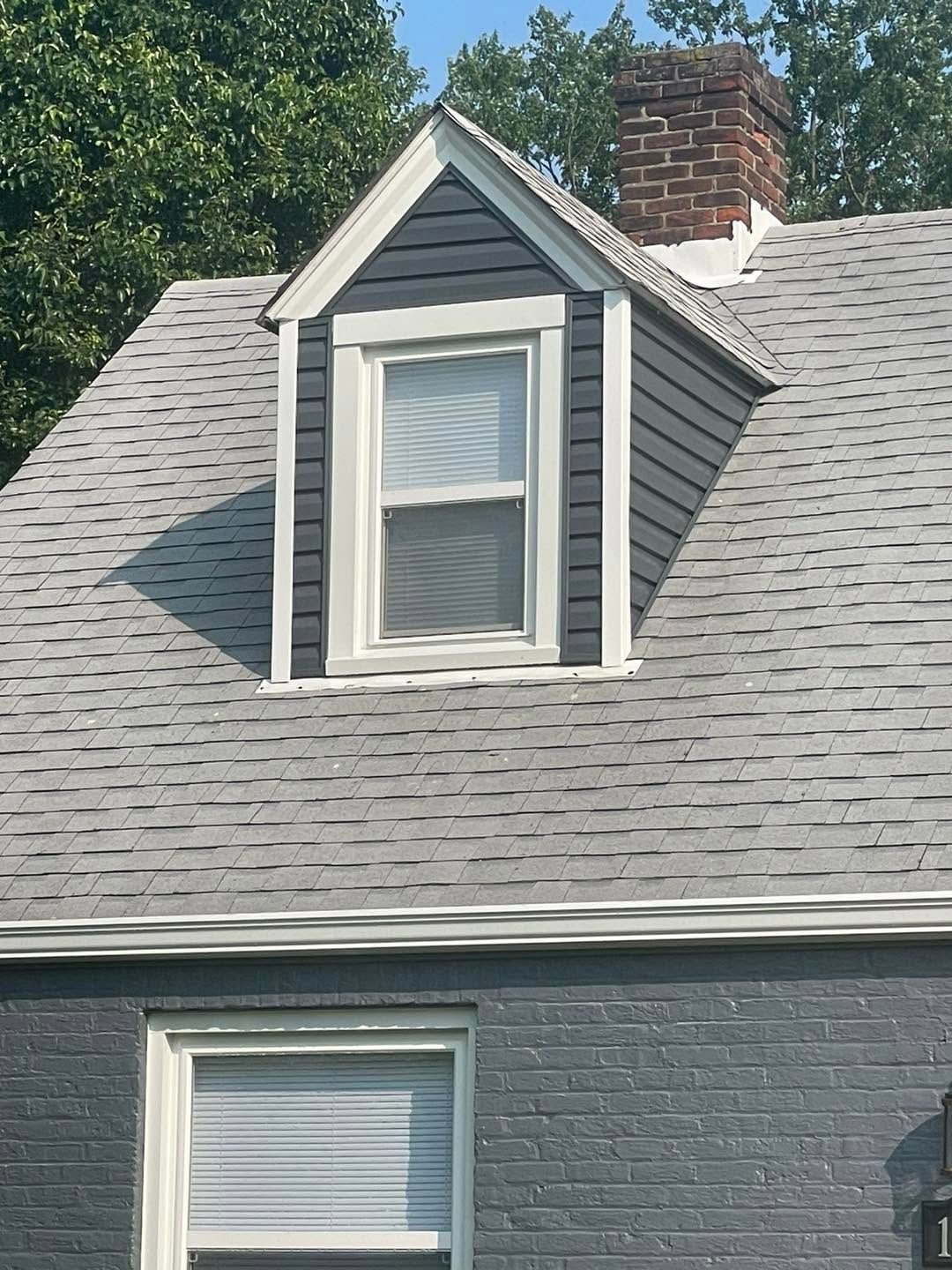 Gray shingled roof with a small dormer window and red brick chimney on a house