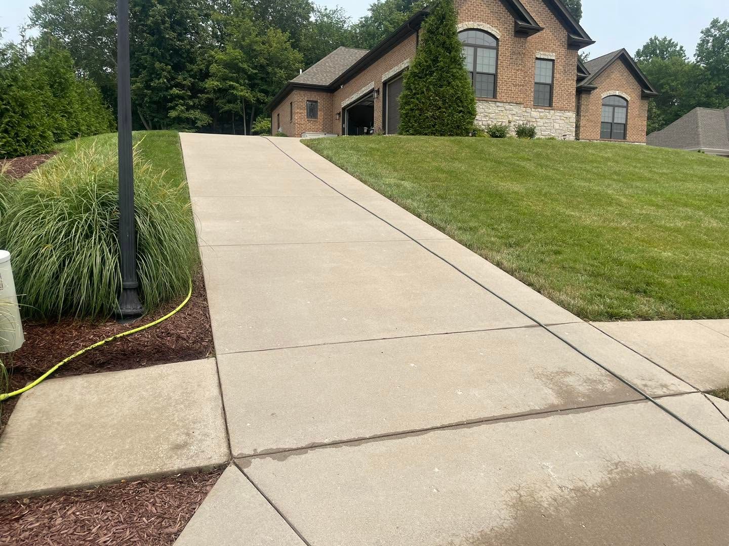 Concrete driveway leading to a brick house on a grassy slope