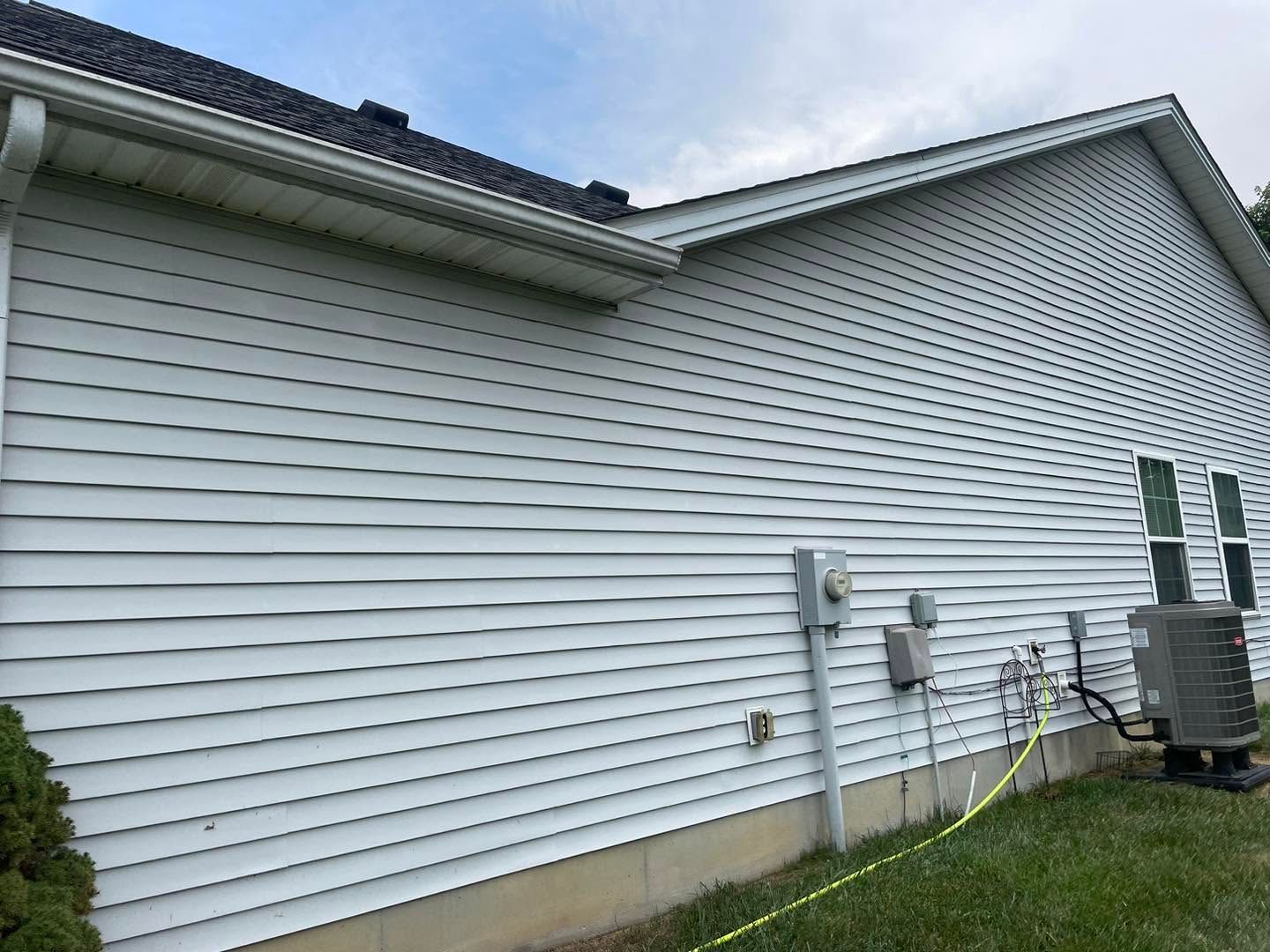 Side of a white house with vinyl siding, utility meters, and air-conditioning units on a grassy yard