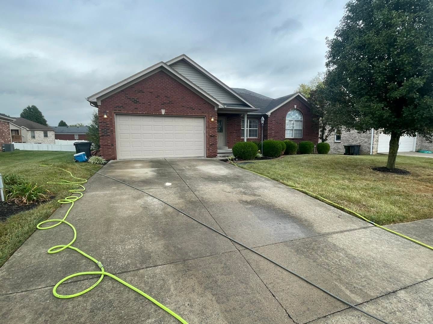 Suburban brick house with a two-car garage, wet driveway, and a green hose across the concrete.