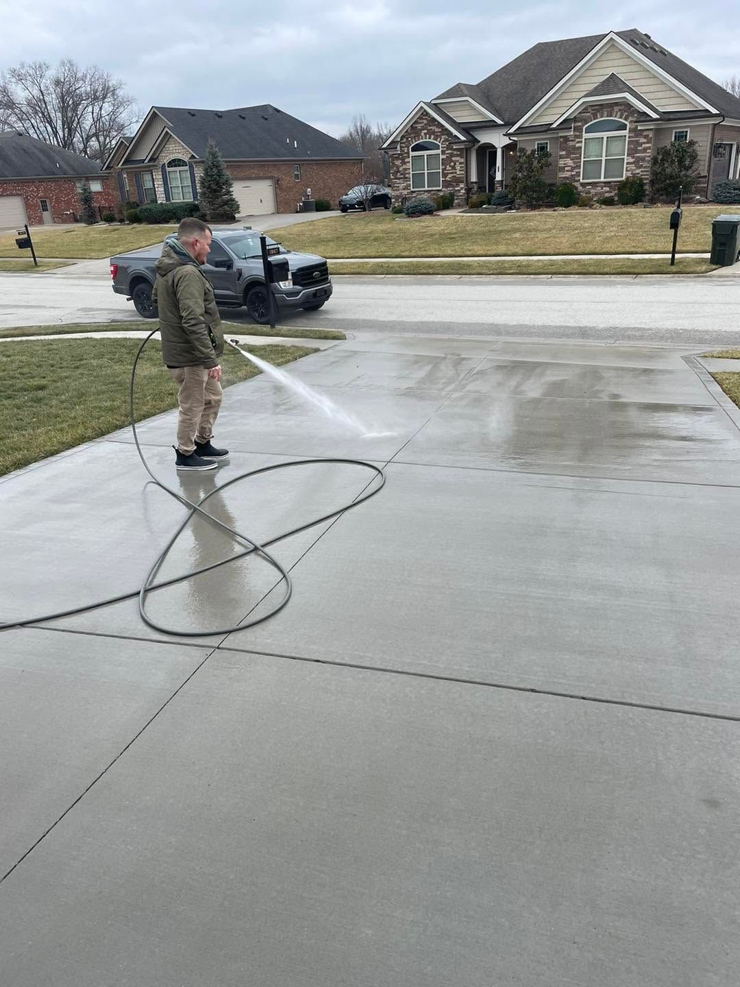 Person pressure-washing a driveway in a suburban neighborhood on a wet, overcast day