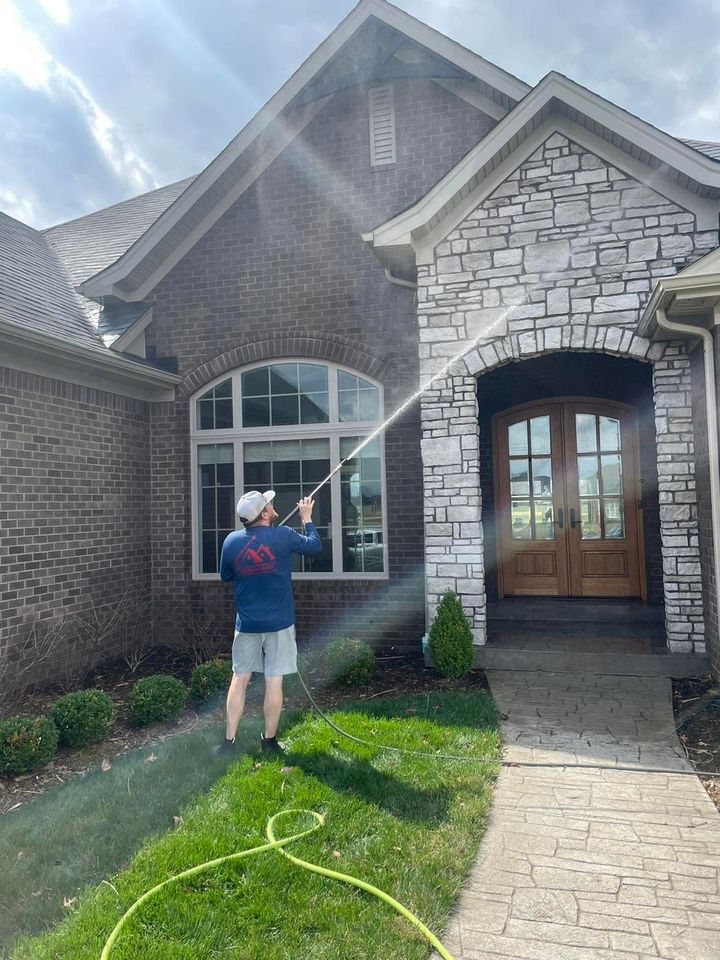 Person spraying water on the front of a stone house with a garden hose