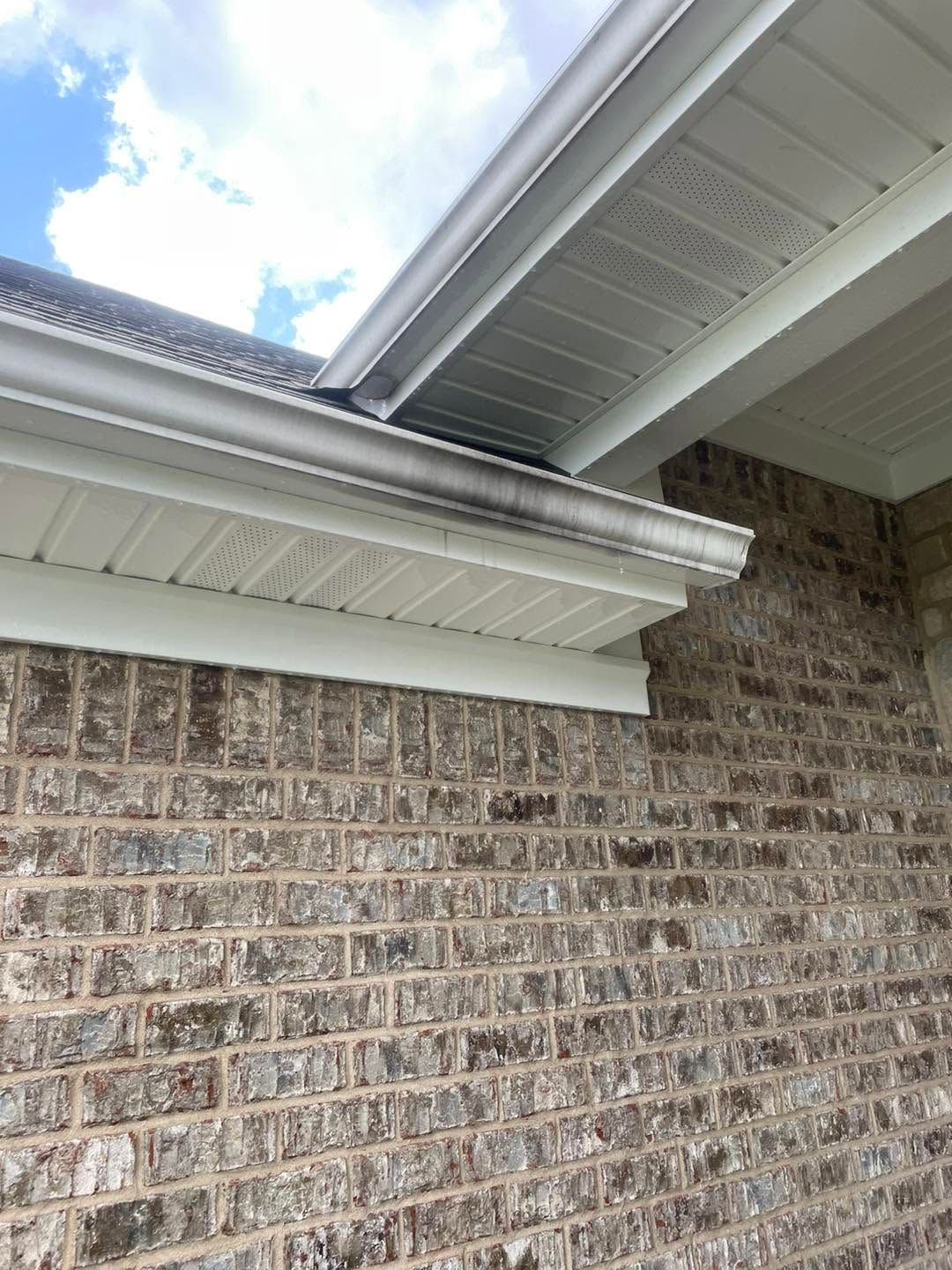 Brick house exterior with white soffit, gutter, and roofline against a partly cloudy sky