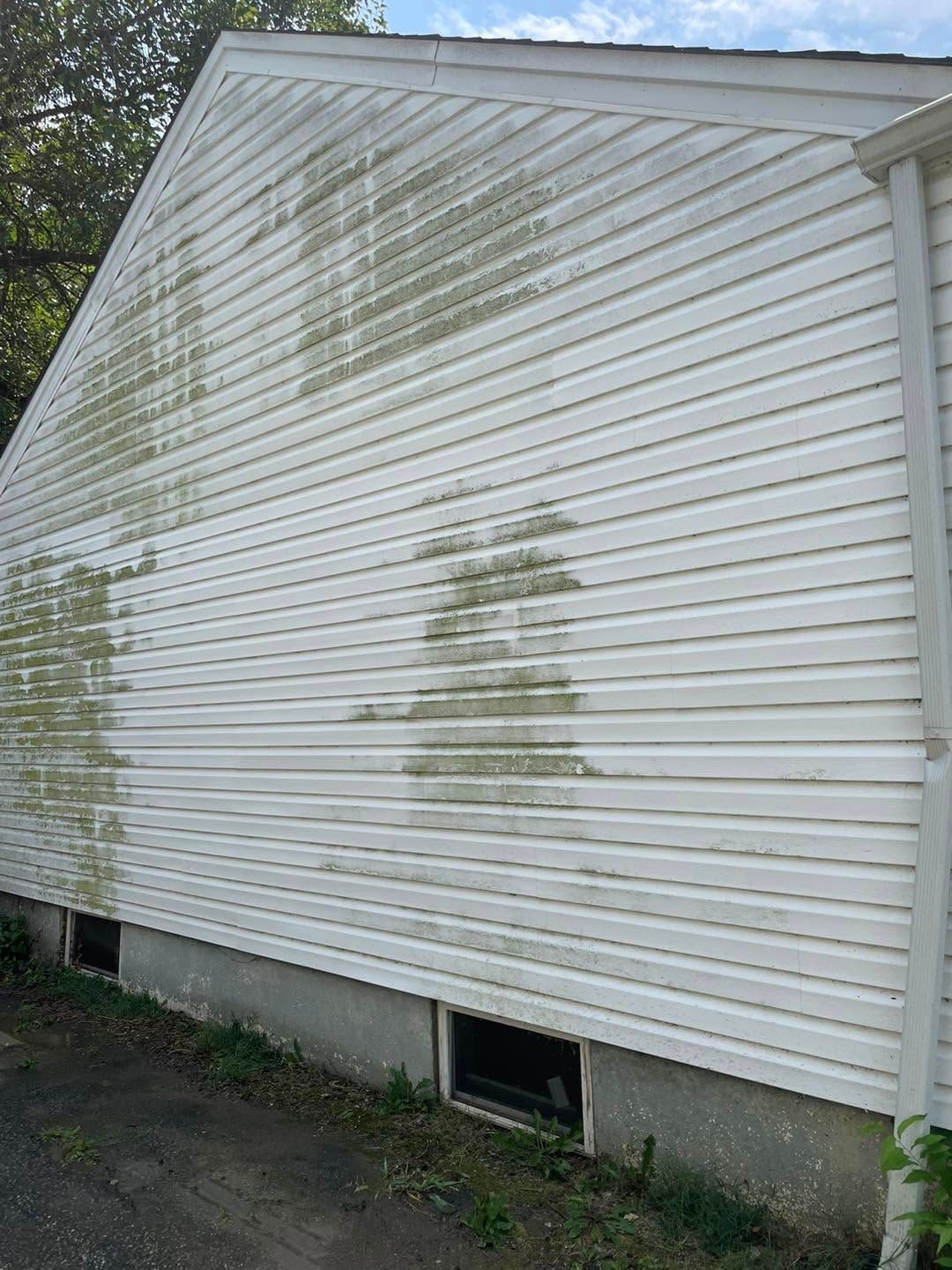 White house siding with green mold or mildew stains and a small basement window near the ground