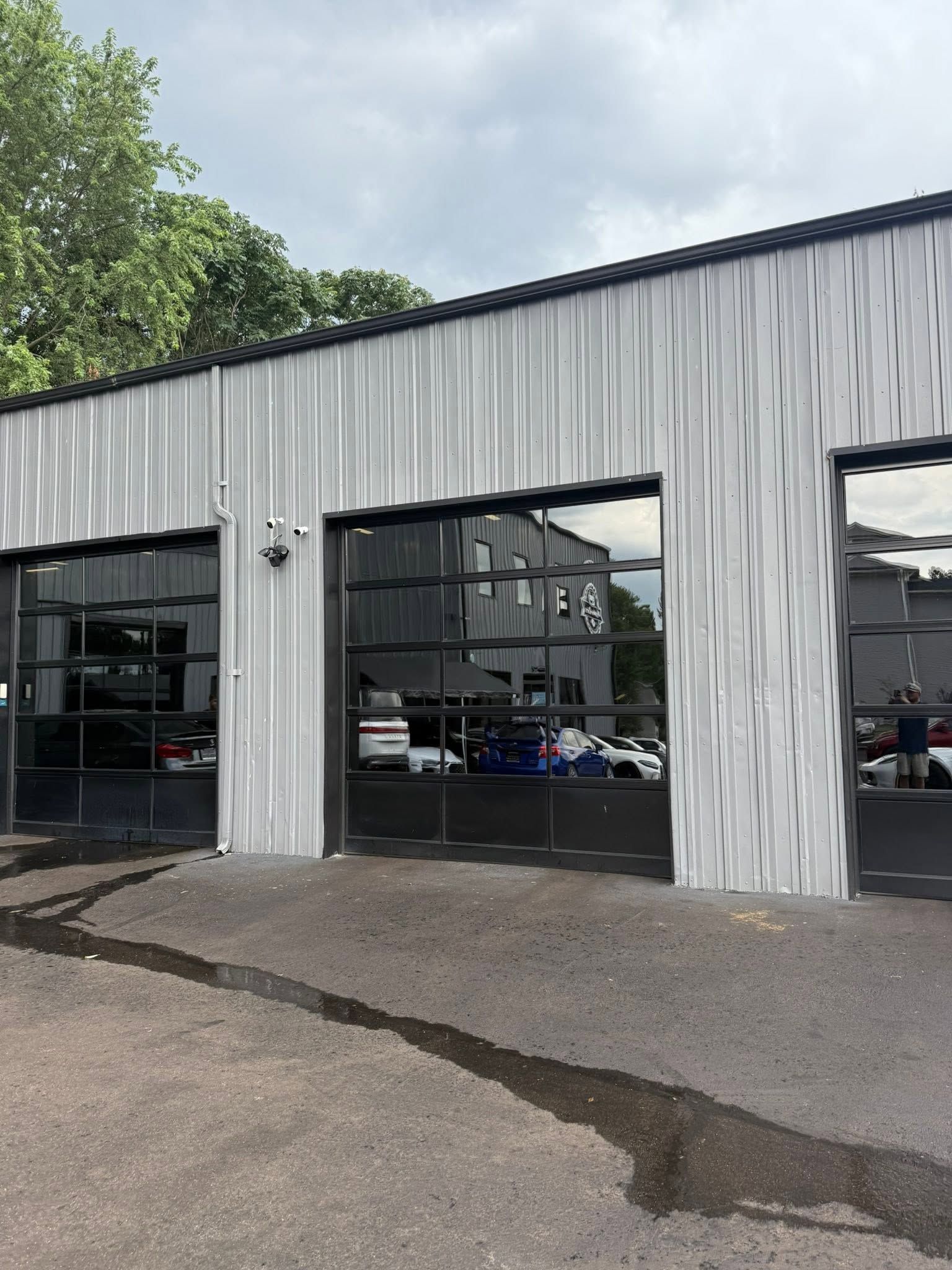 Gray industrial building with open garage bays and parked vehicles inside, viewed from a paved lot.