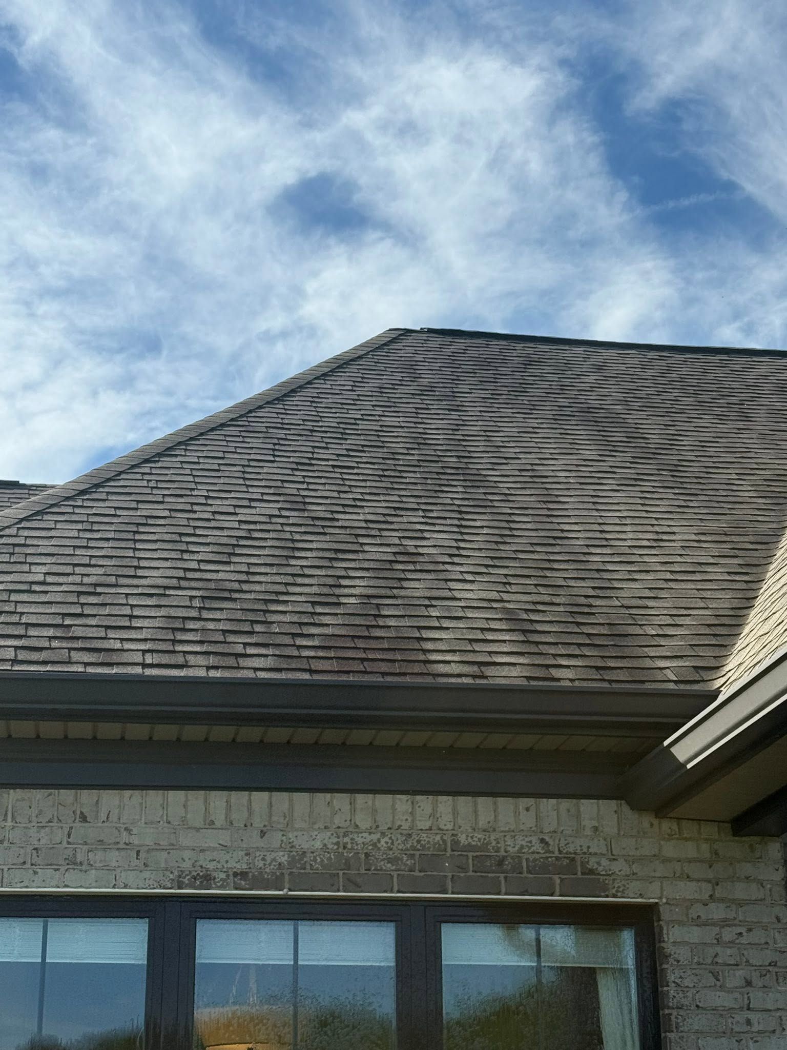 Close-up of a shingled roof above a brick house under a partly cloudy sky