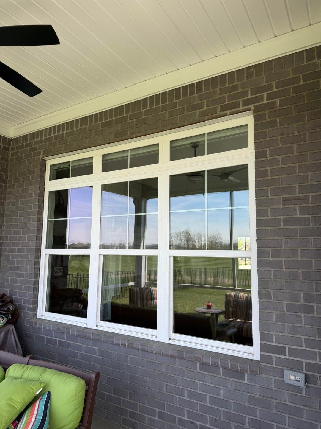 Covered patio with white-trimmed windows and dark brick wall overlooking a green yard