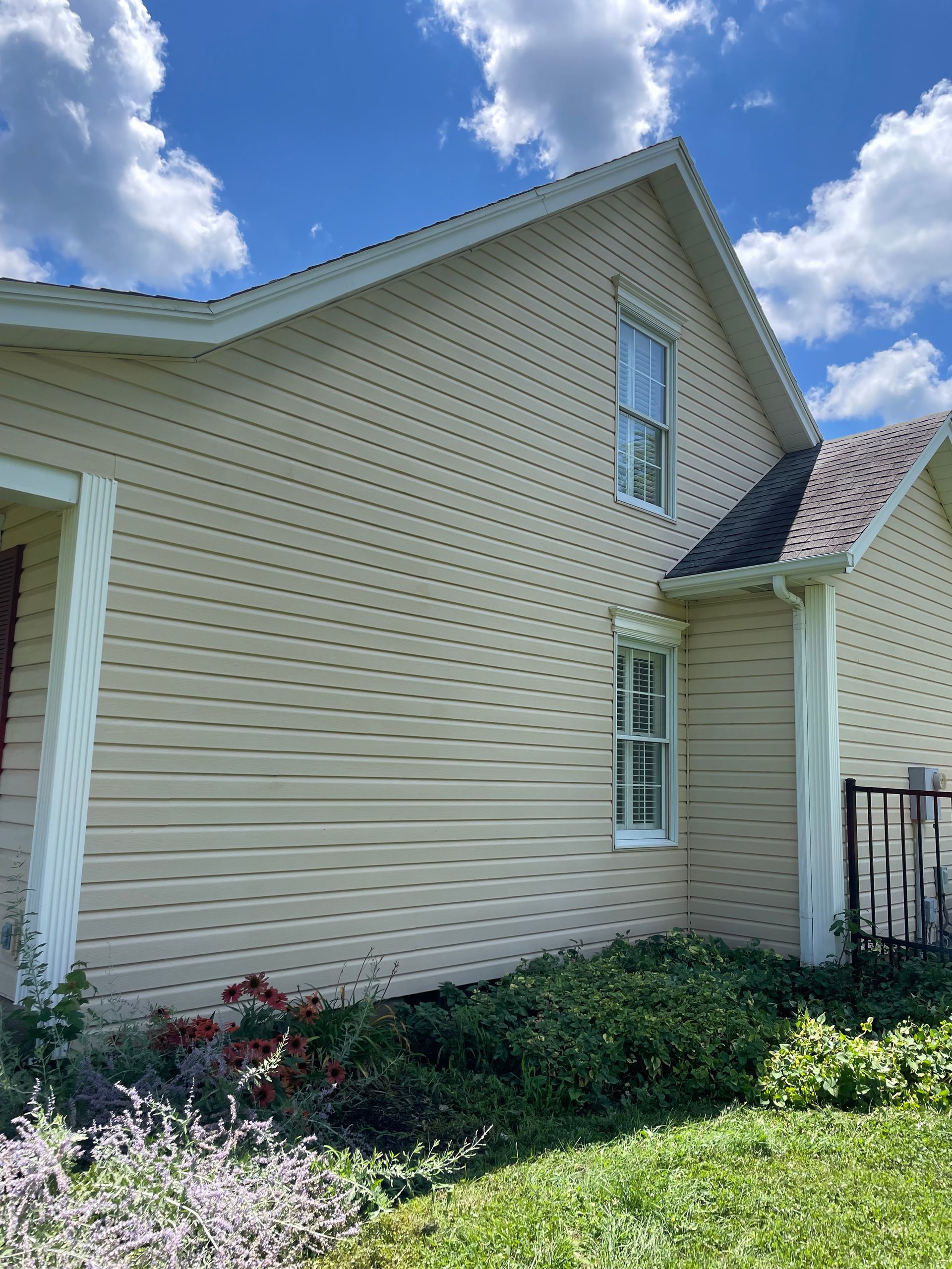 Side view of a beige house with white trim, a small porch, and a blue sky with clouds above.