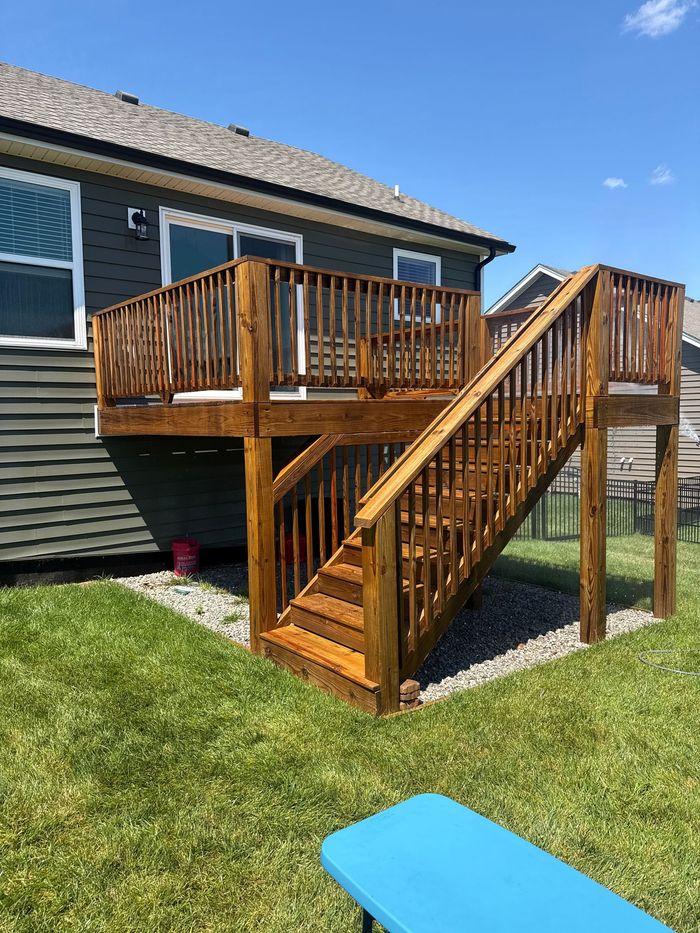 Wooden raised deck with stairs on the side of a house in a sunny backyard
