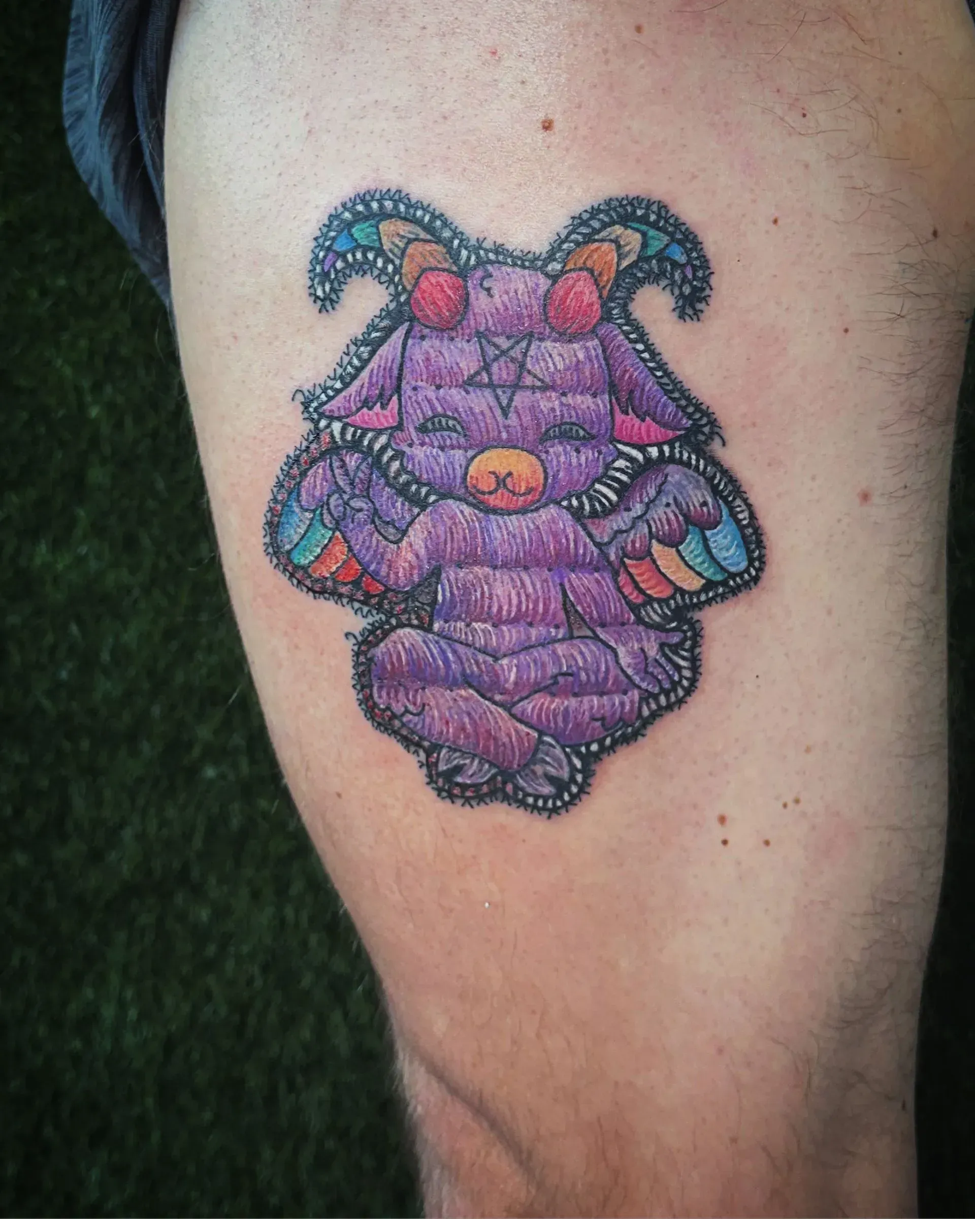 Purple cartoon cat tattoo on a person's upper arm with teal horns and an orange nose.