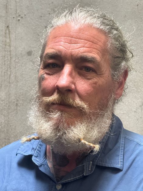 Portrait of a bearded man in a blue shirt against a gray wall