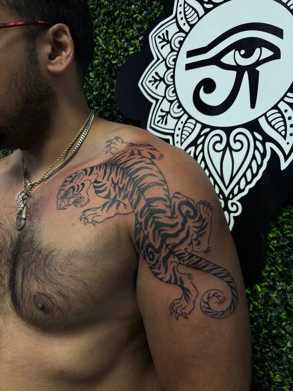 Man's tattooed upper torso and shoulder beside a black-and-white Eye of Horus wall design
