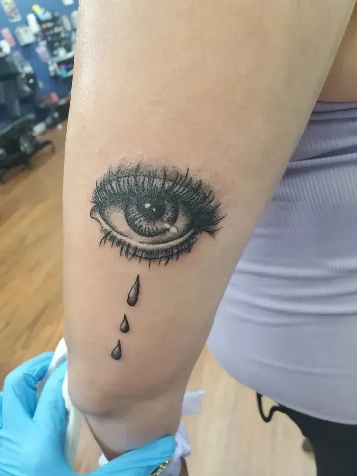 Black eye tattoo with three teardrops on a person’s forearm