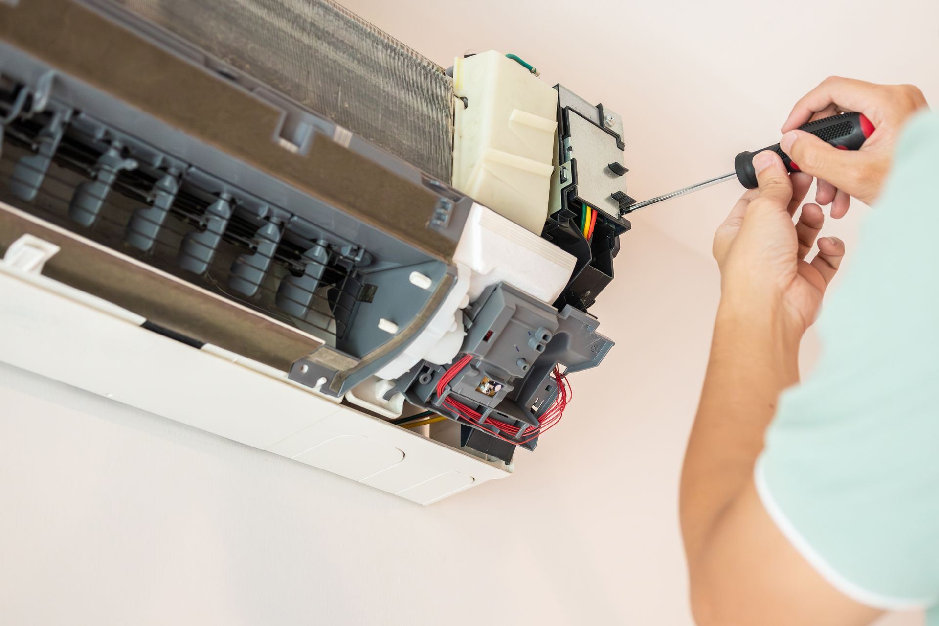 Person repairing a white air conditioning unit with a screwdriver.