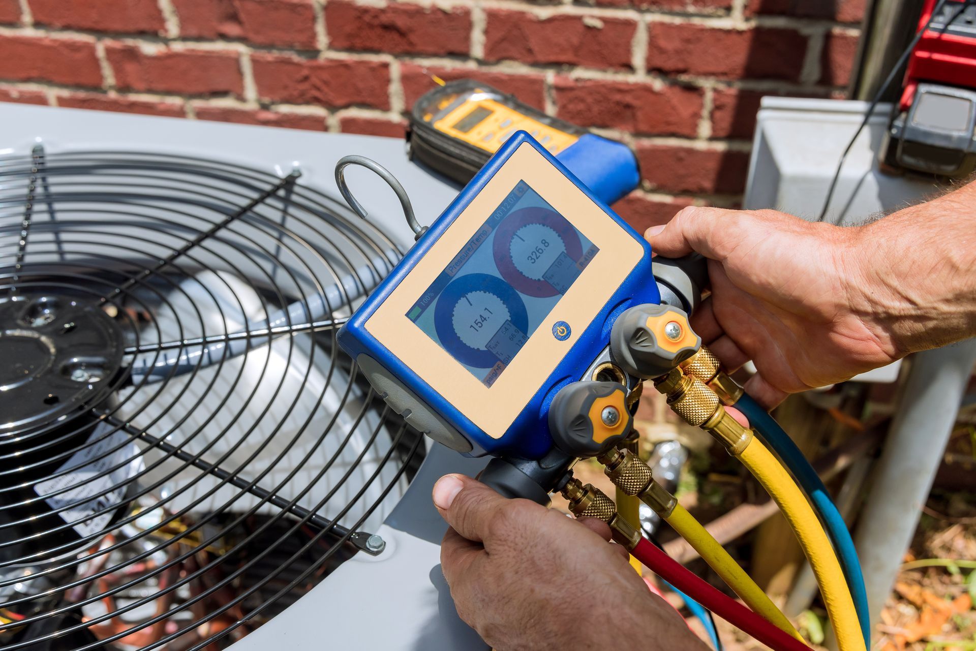 Person using a digital HVAC gauge to check an air conditioning unit; hoses are connected to the unit.