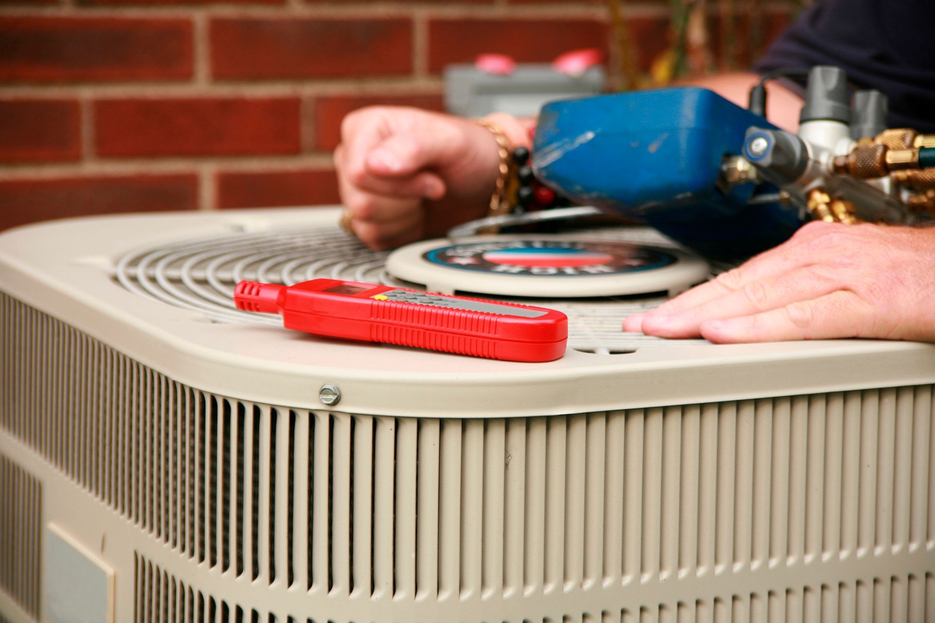 HVAC technician repairs an air conditioning unit; tools on top, brick background.