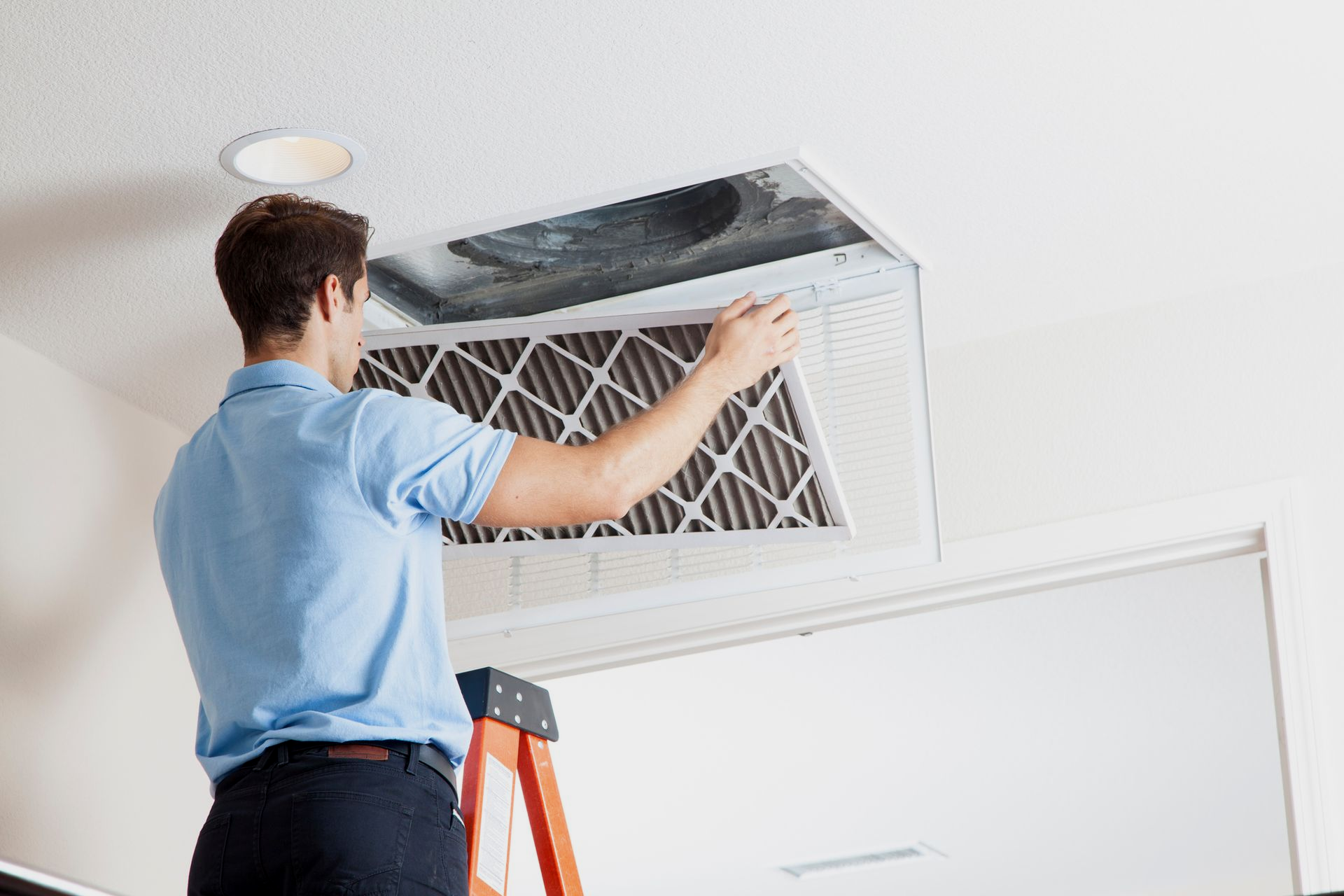 Person on a ladder changing an air filter in a ceiling vent.