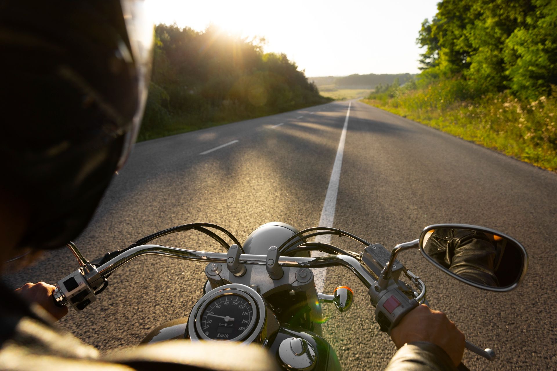 Motorcycle rider on a sunlit country road, seen from the handlebars