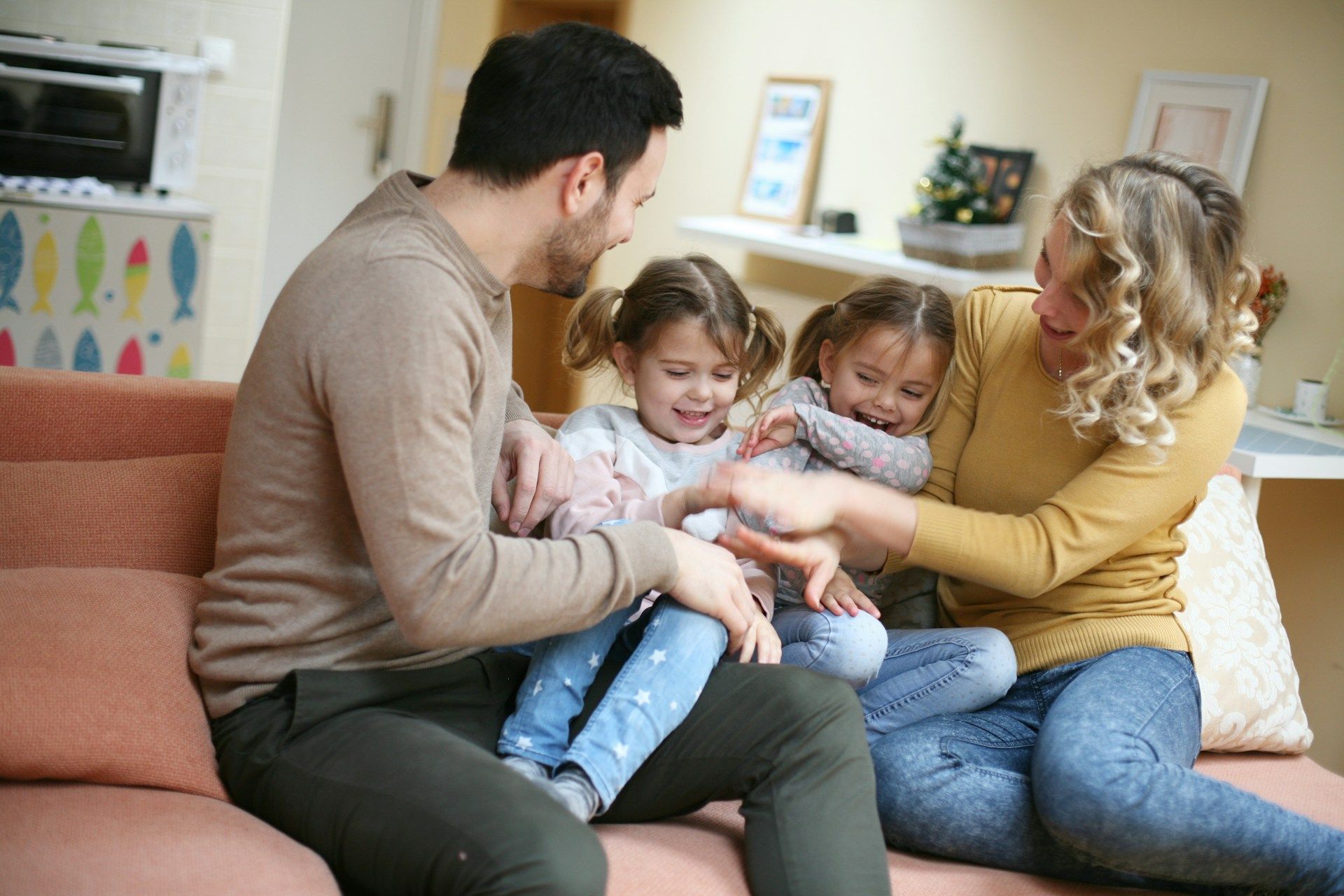 Family sitting on a couch, smiling and playing with two young children in a bright living room
