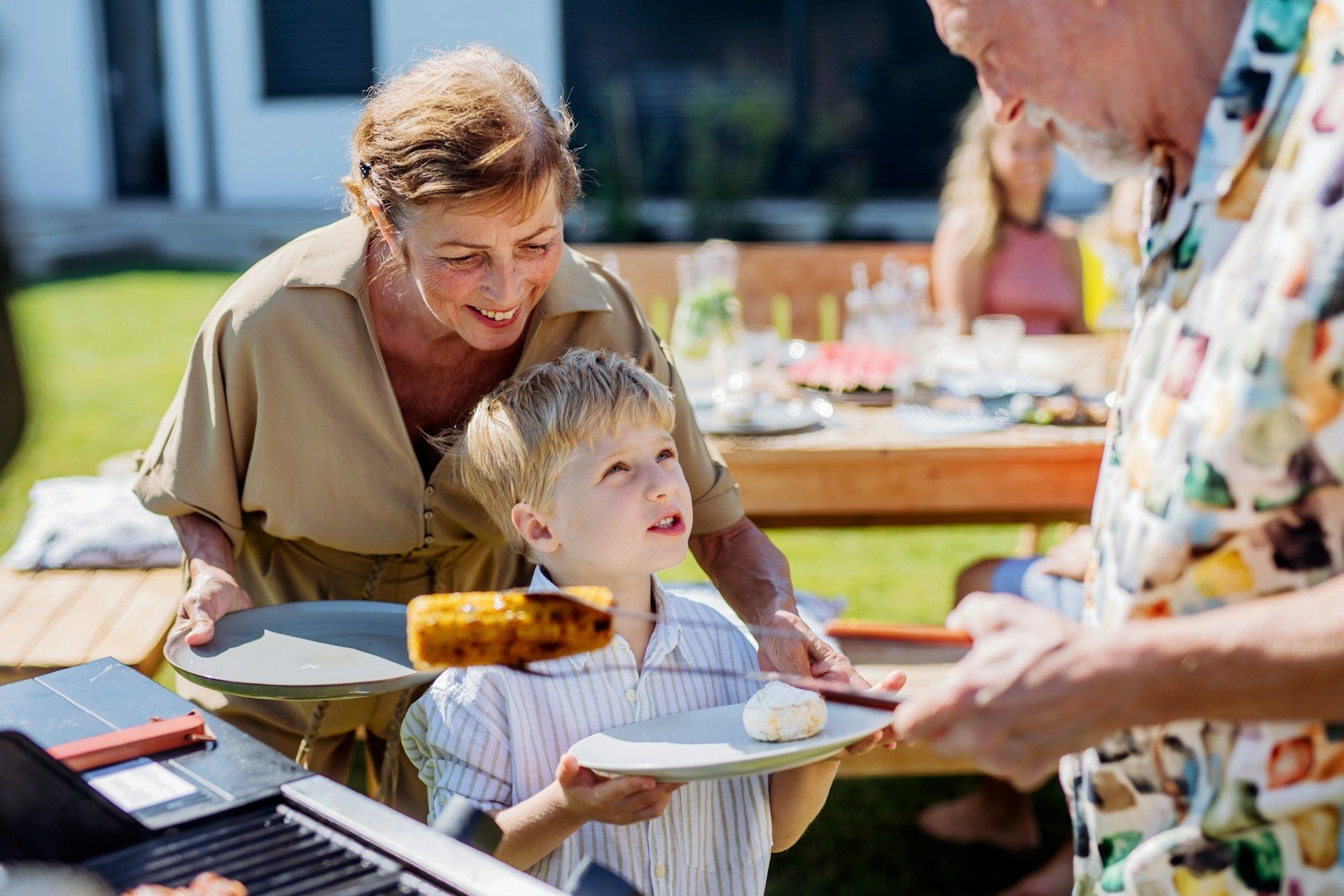 People grilling and serving food at an outdoor picnic table in bright sunlight