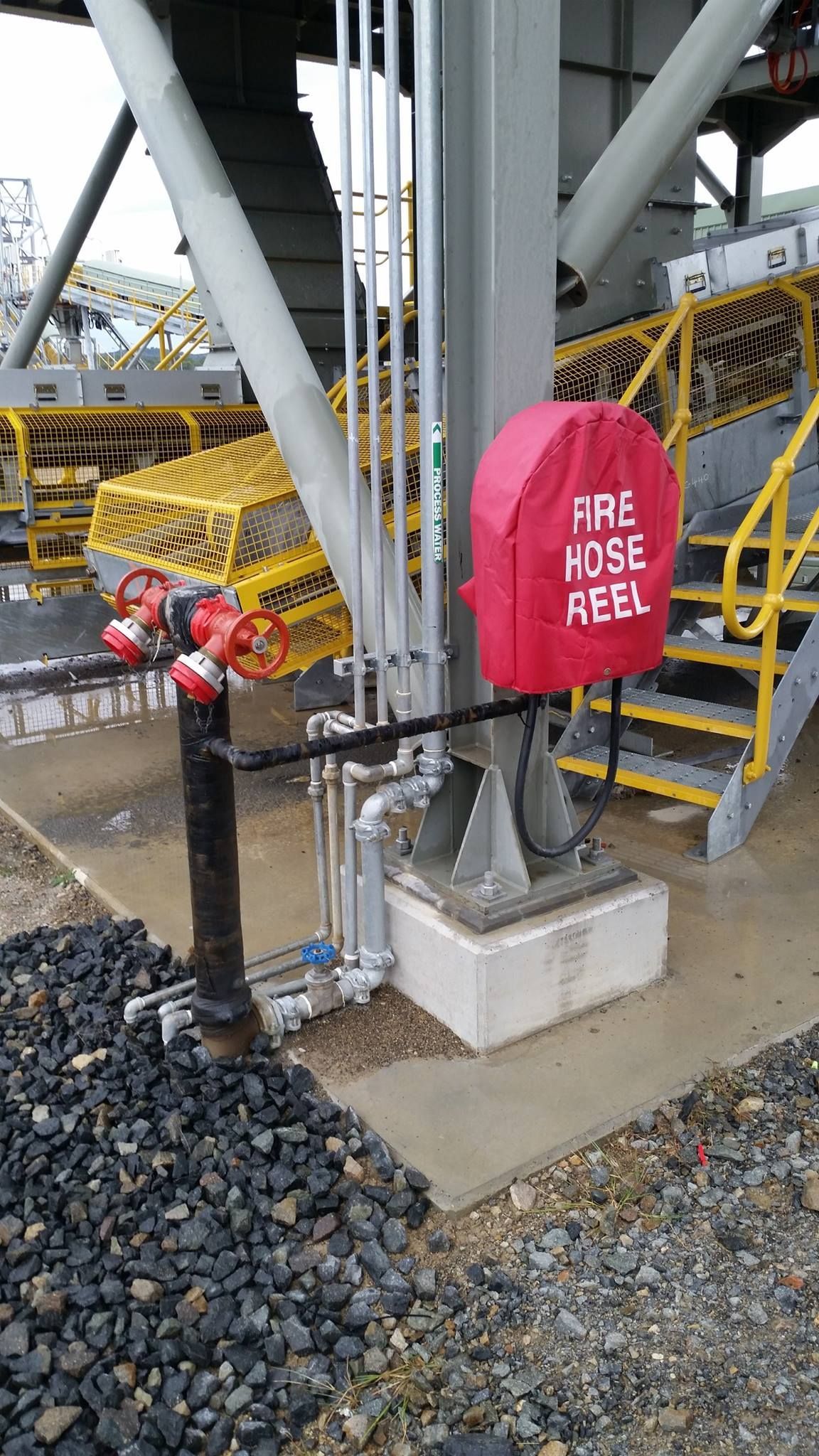 A red fire hose reel is sitting on the ground next to a staircase. A red fire hose reel is sitting on the ground next to a staircase.