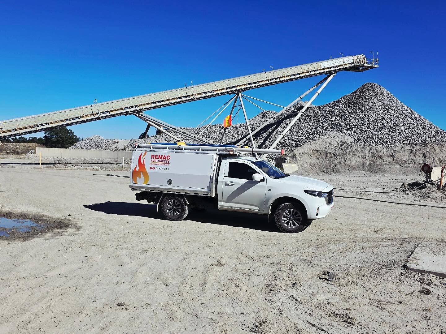 A white truck is parked in the dirt in front of a conveyor belt. A white truck is parked in the dirt in front of a conveyor belt.