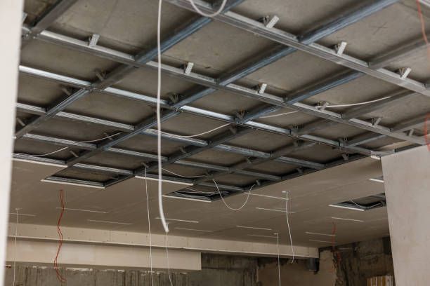 Ceiling construction showing metal grid framework and drywall panels. Wires hang down.