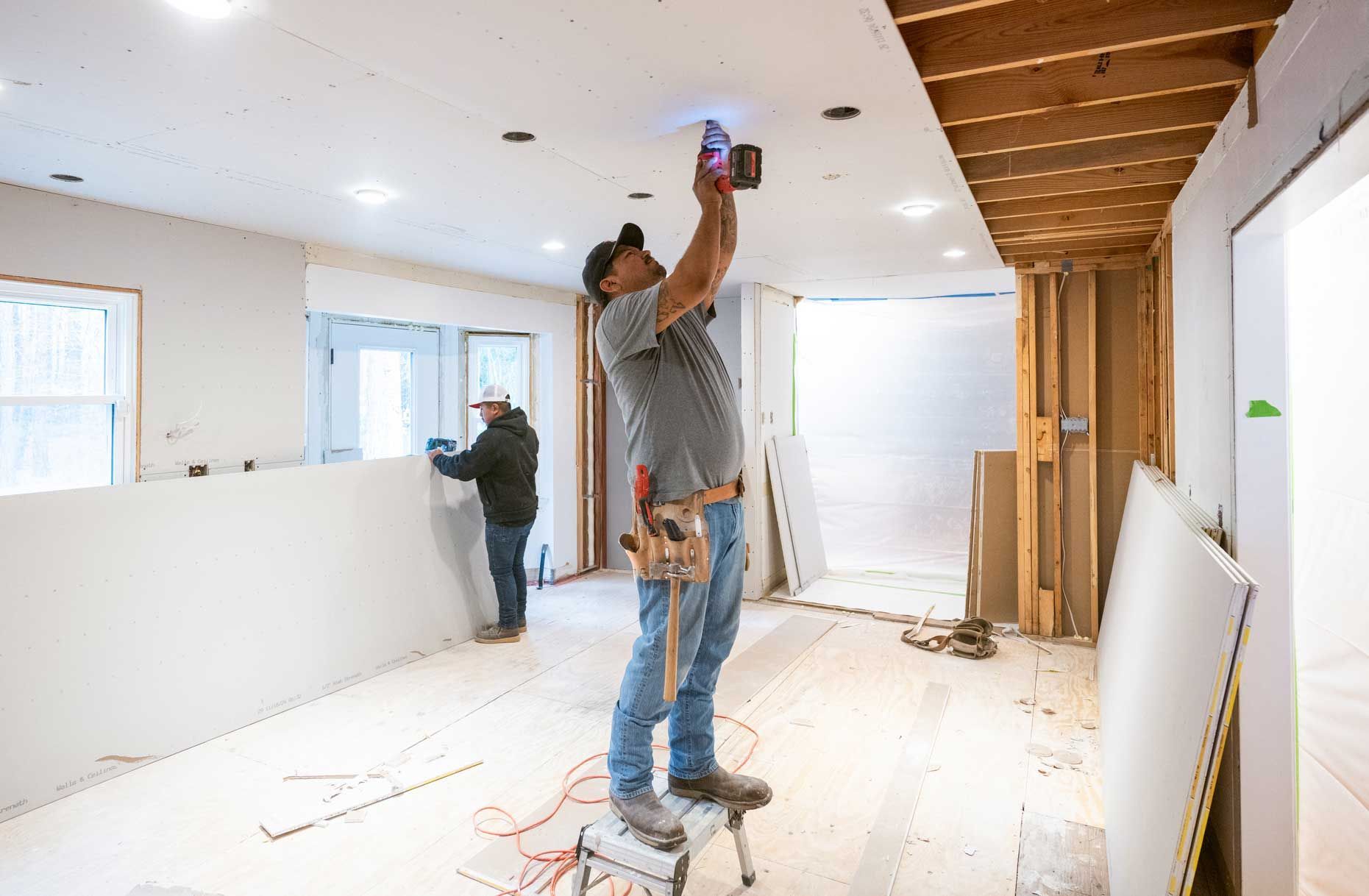 Construction workers installing drywall on a ceiling inside a home during renovation.